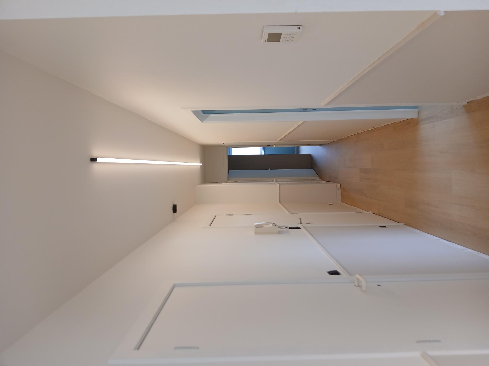 Strakke lijnverlichting tegen het plafond van een gang, met bedieningspaneel aan de wand