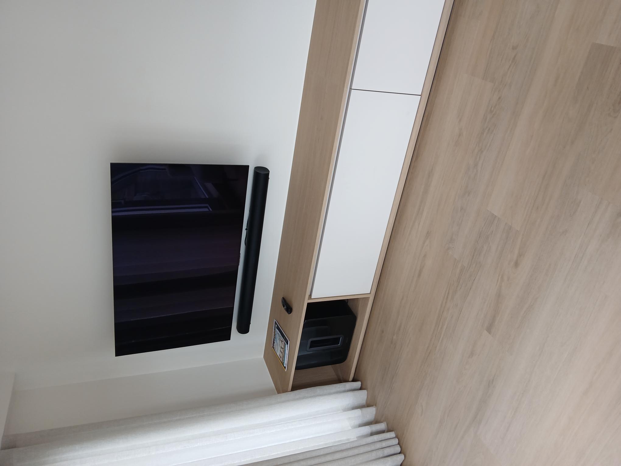 Wandgemonteerde televisie met soundbar boven een houten tv-meubel, met weggewerkte bekabeling